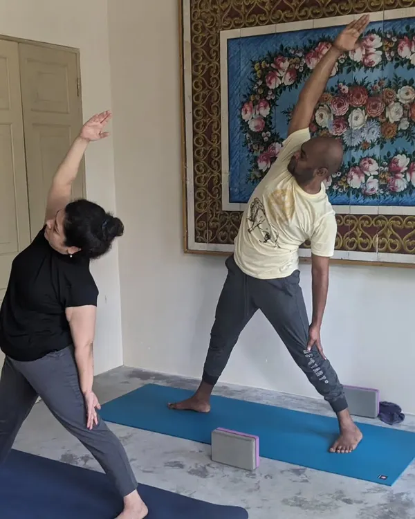 Two students moving through Trikonasana, or Triangle Pose, during an indoor session on our retreat. Even when we practice inside, the focus is on mindful movement and supporting each other's journey.