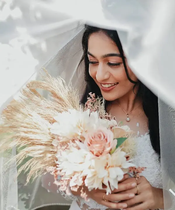A Christian bride smiles softly under her veil, holding a beautiful bouquet. I use natural light to create these dreamy, romantic bridal portraits.