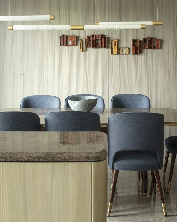 The dining area at the Jor Bagh Residence, featuring a custom table, midnight blue upholstered chairs, and Makrana marble tube lights. A sculptural wall installation adds an artistic layer to the space.