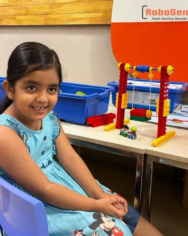 A kindergarten student from our summer camp sits with the functional LEGO swing set she built. This project helps young learners understand concepts of physics and structure in an intuitive, engaging way.