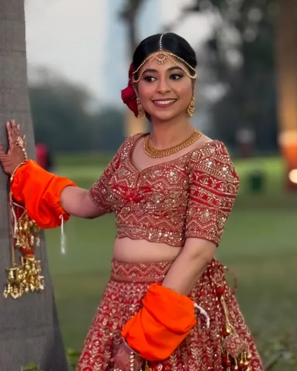 A beautiful outdoor shot of my bride, looking radiant and happy. Her classic red lehenga is paired with soft, glowing makeup.