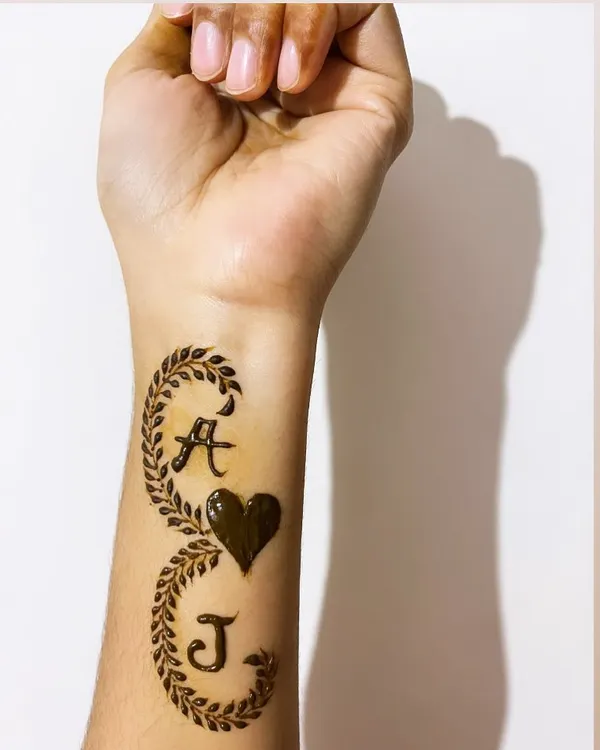 A personalized henna design featuring the initials 'A' and 'J' intertwined with a heart and leafy vines.