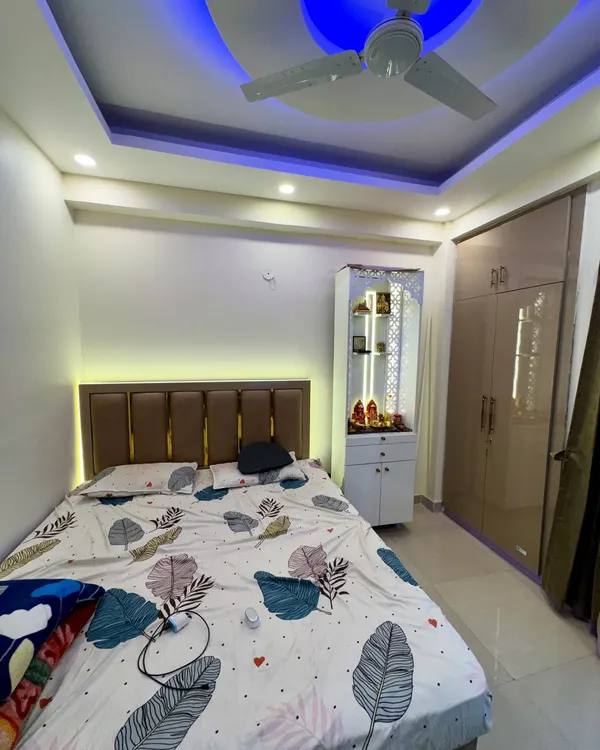 This bedroom includes a compact mandir unit placed neatly beside the wardrobe. The design features jali work and internal lighting.