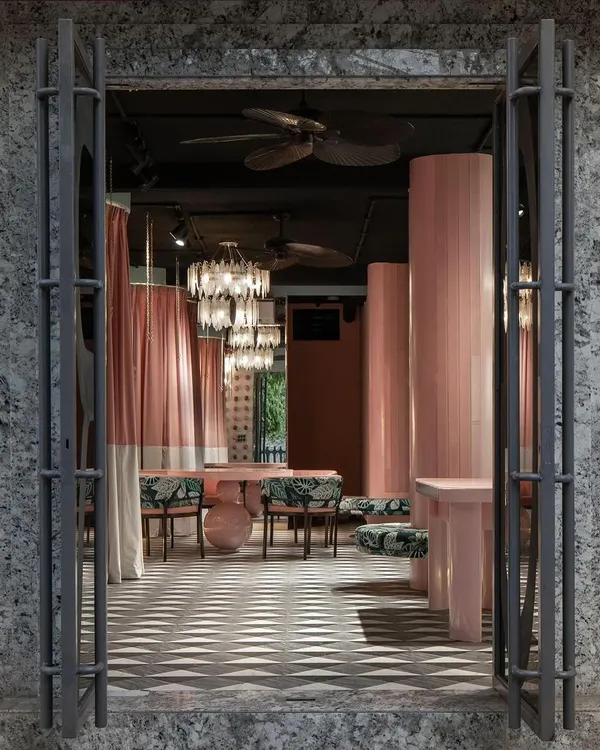 The entrance to this fashion studio frames the interior like a stage. We used heavy, textured doors to create a sense of arrival, opening into a soft, curated world of pink tones, patterned floors, and dramatic chandeliers.