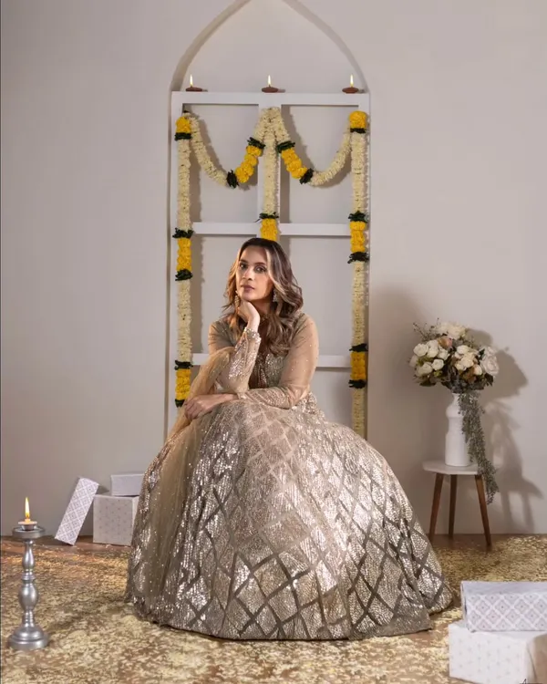 A full-length portrait from a festive studio shoot. The model's elegant pose in a sparkling lehenga, combined with the traditional decor of marigolds and diyas, creates a beautiful and celebratory image.