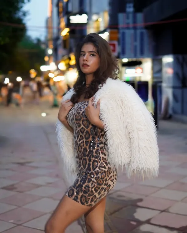 Capturing a bold street style look after dusk. The combination of a leopard print dress and a white faux fur jacket creates a statement against the blurred city lights.