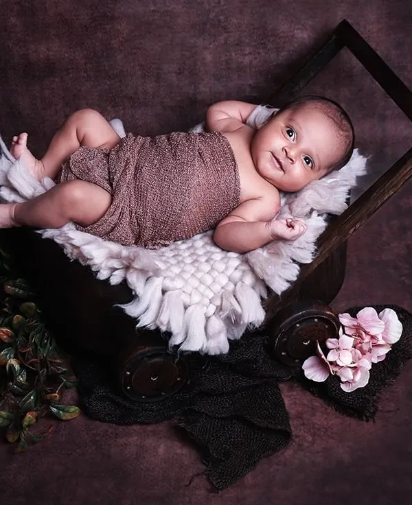 This alert and happy newborn is relaxing in a rustic wooden cart prop. Capturing these awake moments results in engaging and personality-filled portraits.