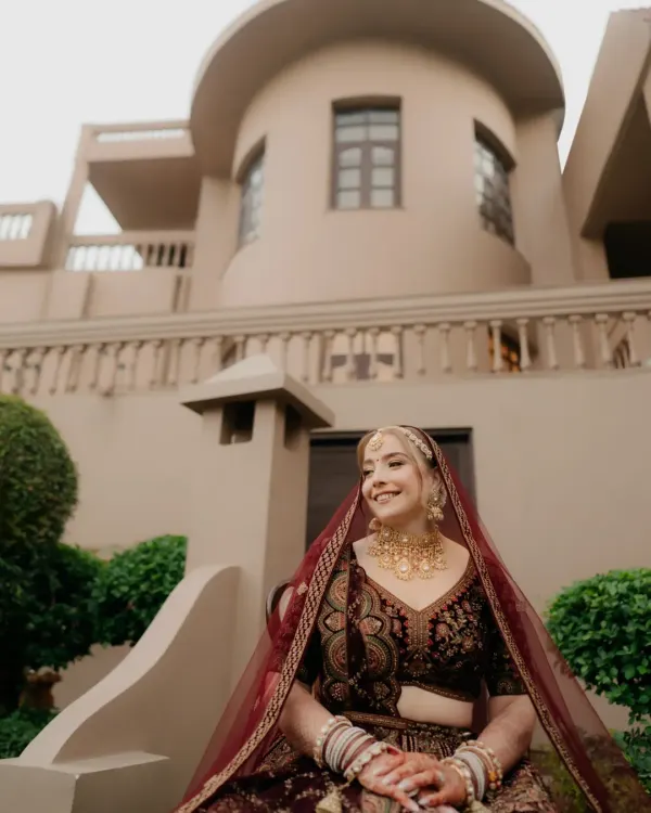 A bride, her eyes filled with stories. This portrait captures her calm, kind, and deep gaze. Her rich maroon lehenga and traditional jewelry are worn with an elegance that is all her own, making for a truly timeless bridal photo.