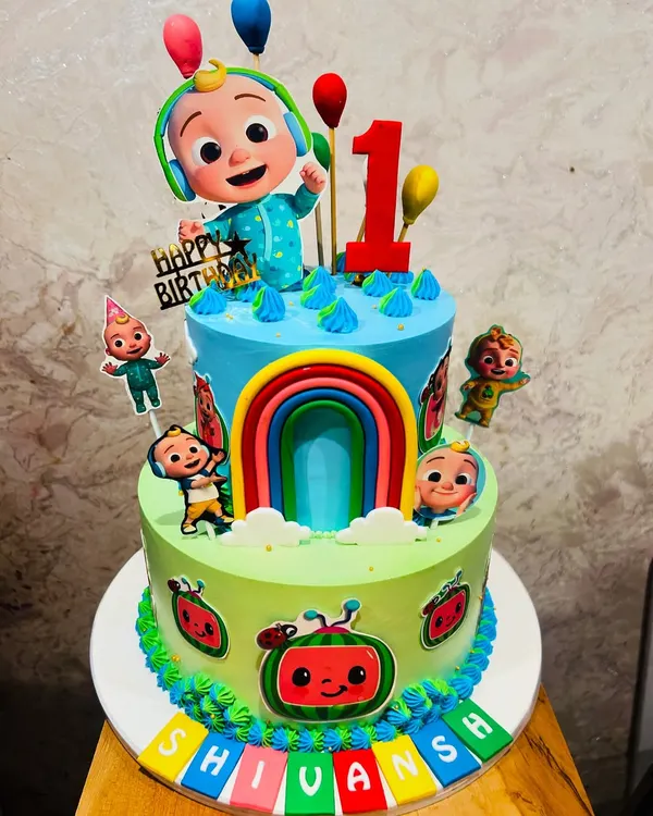 A vibrant two-tier Cocomelon cake, perfect for a first birthday. This colorful creation features JJ and his friends, a rainbow, and bright details from the popular show.