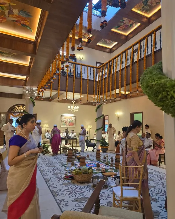 A glimpse into the family home of Sri Veerendra Hegde ji in Mangalore during a ceremony. The design features a double-height space with a coffer slab ceiling, traditional wooden railings, and a large, patterned rug.