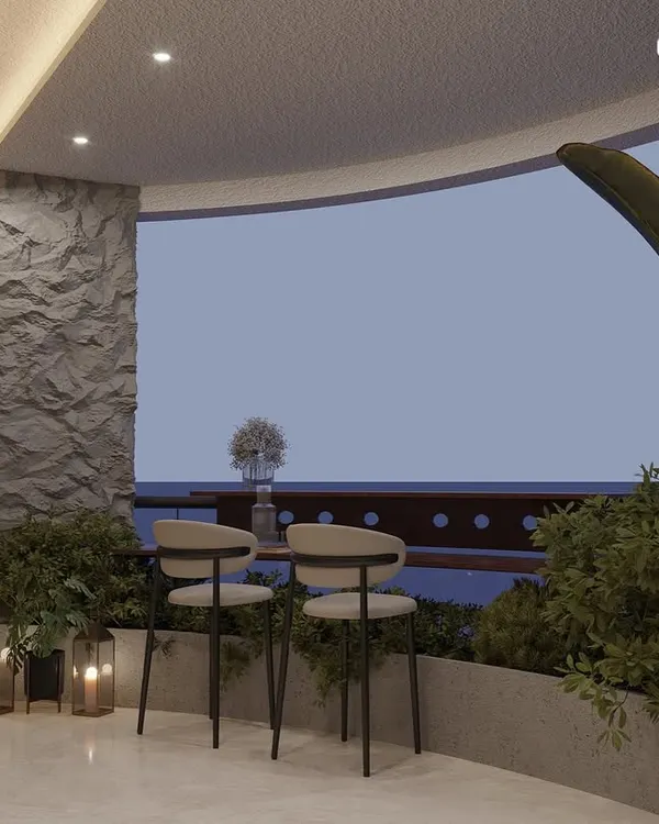 A cozy corner of a curved balcony, designed as a small breakfast nook or coffee spot. The textured stone wall, candle lanterns, and surrounding plants create a warm and intimate setting.