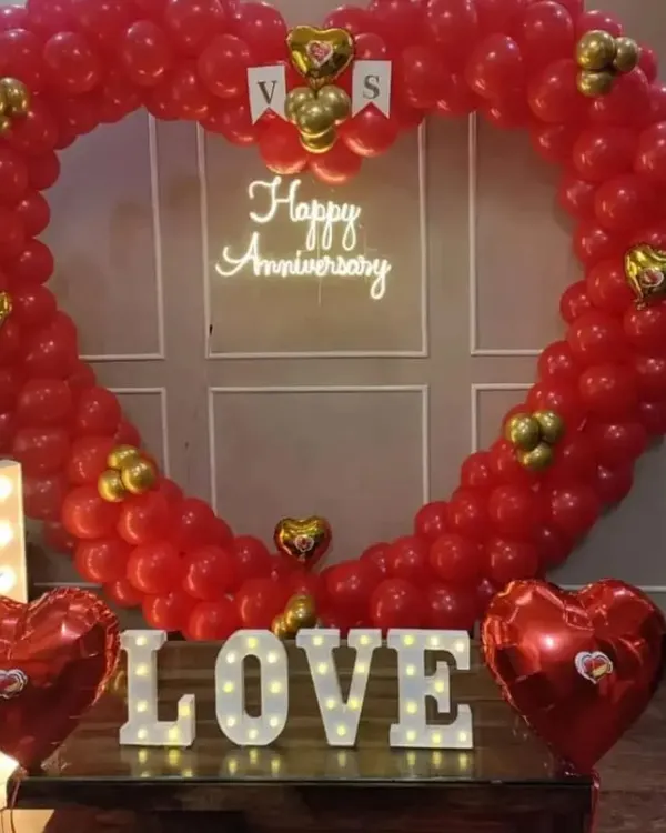 I created this grand heart-shaped balloon arch entirely with red balloons for a first-anniversary celebration. The setup is completed with a 'Happy Anniversary' neon sign, marquee 'LOVE' letters, and heart-shaped foil balloons.