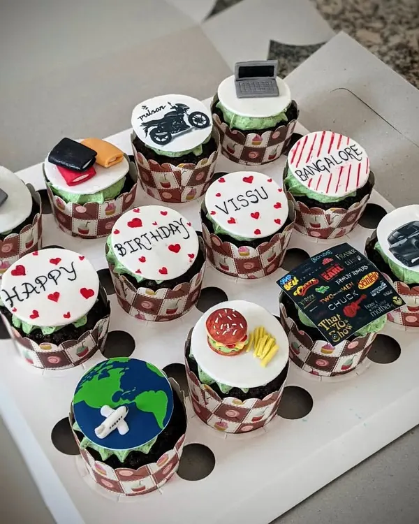 A full set of customized cupcakes, each with a unique, handcrafted topper. Themes here include travel, food, movies, and cars, showing the wide range of personalization possible.