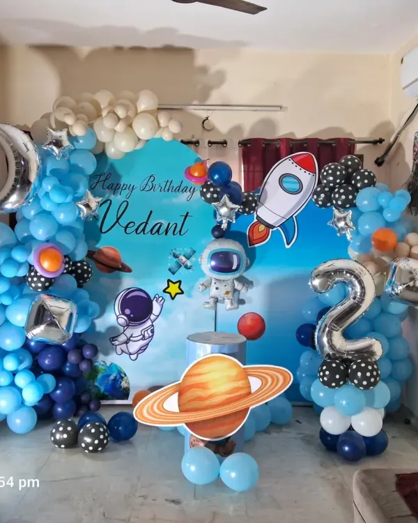 An out-of-this-world space theme birthday party for a second birthday. The setup is complete with a custom backdrop, balloon garlands, and cutouts of astronauts, rockets, and planets.