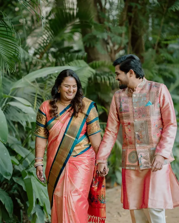 A candid close-up of a couple in beautiful traditional outfits, holding hands and smiling at each other while walking through a park. Their genuine laughter is the focus of this engagement photo.
