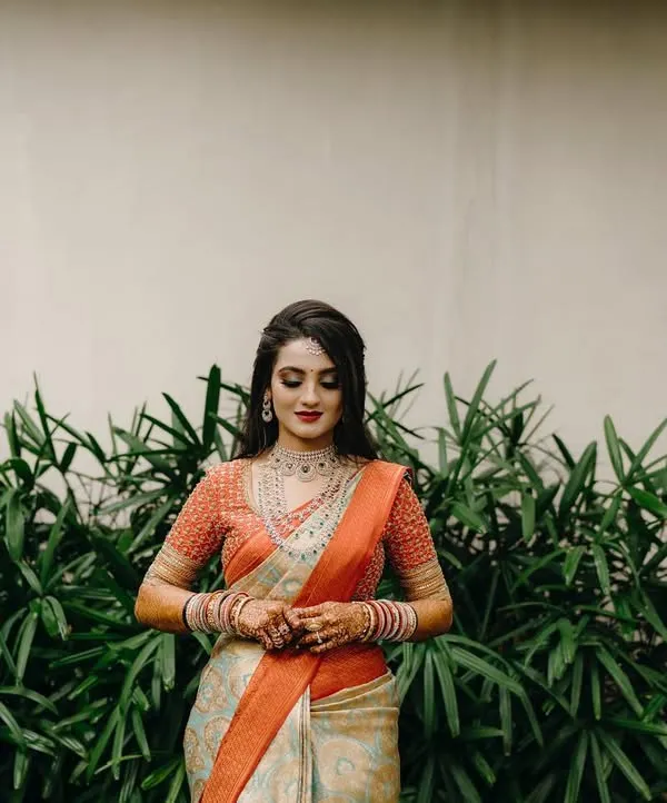 A beautiful solo portrait of a bride in her reception saree, looking down with a gentle smile. The simple background emphasizes her elegance and intricate jewelry.