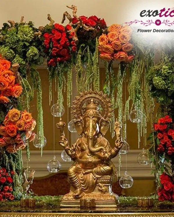 A magnificent golden Ganpati idol framed by a lush, modern arch of red and orange roses, fresh greenery, and delicate hanging glass orbs. This premium Ganpati decoration blends traditional devotion with contemporary elegance, creating a truly divine centerpiece for your festival.