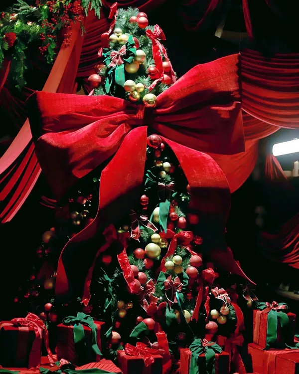 A magnificent Christmas tree adorned with a giant red velvet bow, red and gold ornaments, and surrounded by beautifully wrapped presents. This is the centerpiece of a dramatic, all-red holiday theme.
