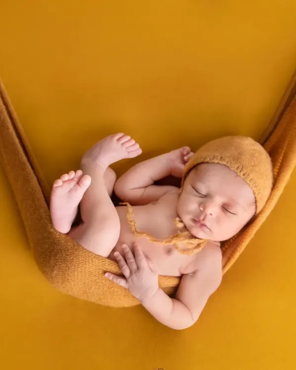 A classic newborn pose, with the baby sleeping peacefully in a mustard-colored sling against a matching backdrop. This highlights the simple, artistic style of my newborn photography.