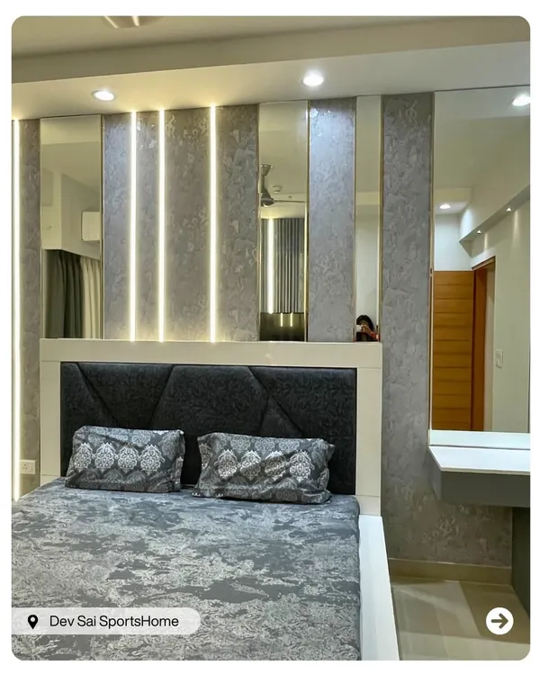 This master bedroom features a dramatic back wall with textured grey panels, vertical light strips, and mirrors to create an illusion of space. The geometric upholstered headboard adds a modern, luxurious touch.