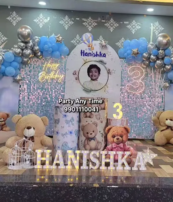 This is my complete teddy bear theme for a 3rd birthday party. It includes a custom backdrop with a photo, a shimmer wall, a balloon arch in blue and silver, themed plinths for the cake, and light-up marquee letters for the name. I also provide the large teddy bears to complete the look.