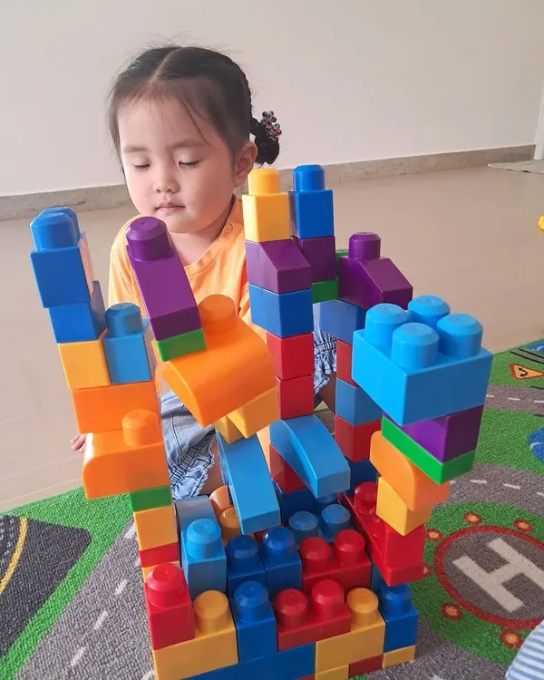 Using large, colorful blocks, this child builds a complex, multi-level structure. This type of open-ended play encourages imagination and develops foundational engineering skills.
