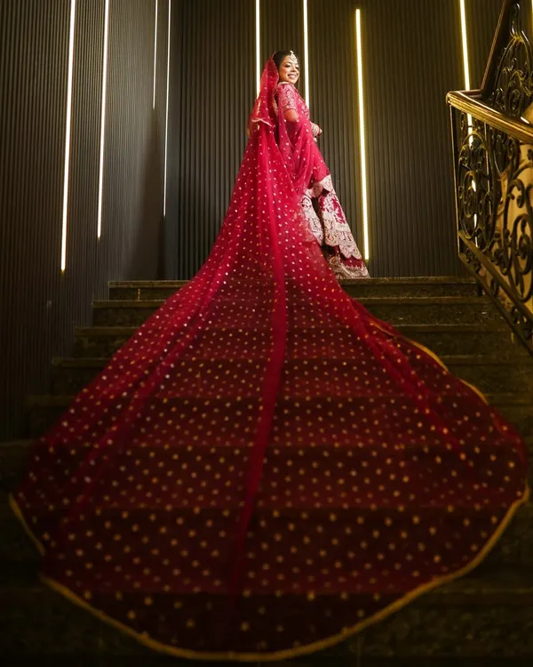 A breathtaking shot of the bride on a staircase, showcasing the magnificent trail of her red wedding lehenga. This kind of dramatic portrait makes a stunning album centerpiece.
