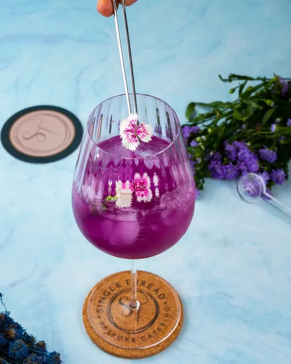 This is 'The Butterfly Effect,' a stunning cocktail made with elderflower-infused gin, butterfly blue pea flower, and lime. Its vibrant purple hue and delicate floral garnish make it as beautiful as it is intoxicating.