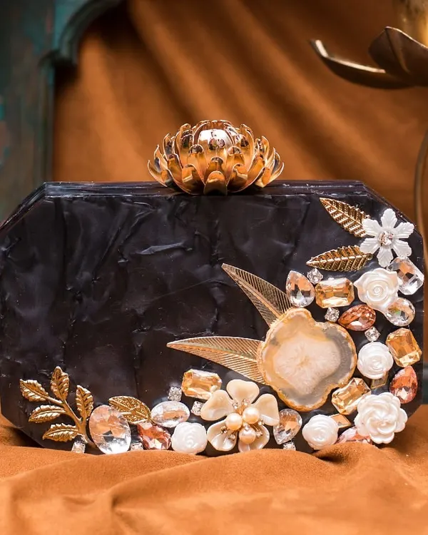 This black acrylic clutch is the definition of evening glamour. It's embellished with golden leaves, white 3D florals, and sparkling stones, all centered around a beautiful agate slice.