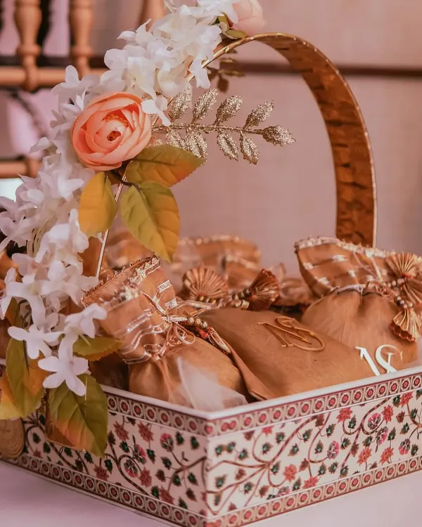 A beautifully arranged favor basket for a Roka ceremony. The basket itself features intricate traditional patterns, filled with monogrammed gift pouches for the guests to take home a piece of the celebration.