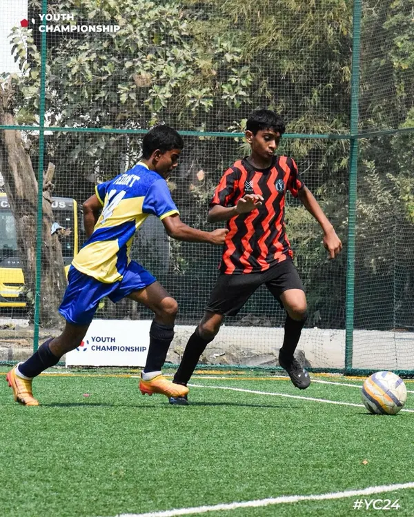 A young player in our red and black zig-zag kit skillfully maneuvers the ball past a defender during the Youth Championship 2024.