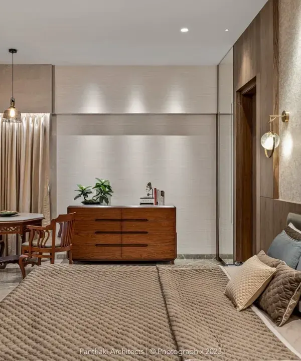 This master bedroom is designed as a refined retreat. It features a comfortable bed with an upholstered headboard, a separate seating area by the window, and custom-built wooden furniture, all working together to create a space of quiet luxury.
