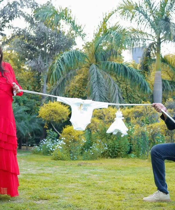 Having some fun during an outdoor shoot. This playful tug-of-war with a clothesline of baby clothes is a creative and lighthearted way to capture the couple's excitement.