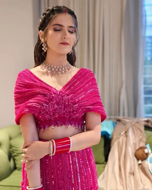 A soft and glowing makeup look for a Sangeet ceremony, with shimmery pink eyeshadow and a natural lip. The braided half-up hairstyle adds a touch of modern elegance to her vibrant pink outfit.