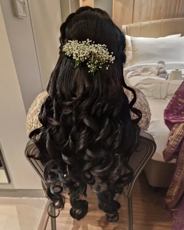 A classic half-up half-down hairstyle featuring voluminous, structured curls and a delicate baby's breath accessory. This look is perfect for wedding guests or bridesmaids seeking an elegant yet soft style.