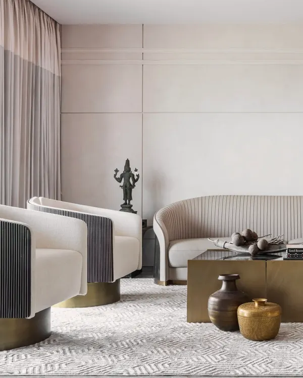 A study in textures and tones. This living space blends vintage brass accents and a traditional bronze statue with modern furniture silhouettes. The pleated sofa, swivel armchairs, and geometric rug create a layered, sophisticated aesthetic.