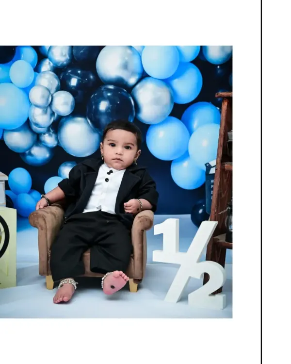 Marking the six-month milestone with a special half-birthday shoot. This little one looks sharp in his suit, sitting confidently in a miniature armchair against a backdrop of blue balloons.