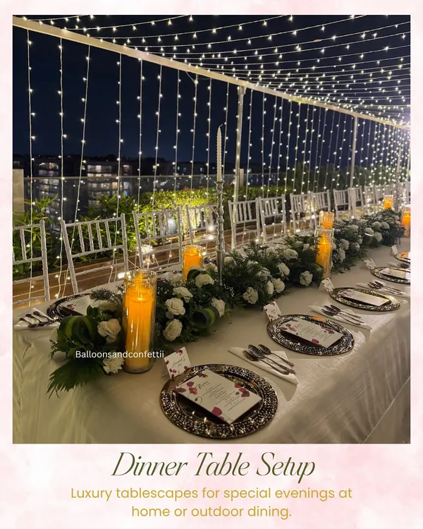 This is the vibe I live for. I transformed a simple rooftop into a magical dining experience under a canopy of fairy lights, perfect for a milestone birthday. The setup features a long table elegantly dressed with lush white floral runners and warm candlelight, creating an unforgettable, luxurious ambiance.