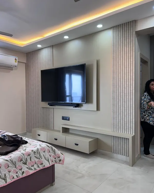 A modern bedroom TV unit with fluted paneling and a floating console. The design incorporates both open shelves and closed drawers for versatile storage.