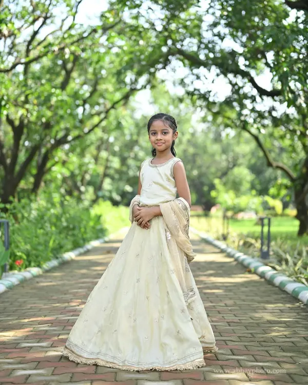 A young girl looking angelic in a custom ivory lehenga. This full-length shot in a park setting shows the beautiful simplicity and elegance of our kids' collection.