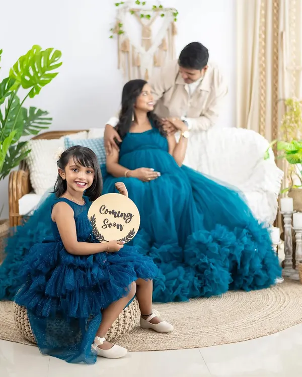 A beautiful family portrait celebrating a new arrival. We love capturing these moments where older siblings, like this excited big sister holding a 'Coming Soon' sign, get to be part of the maternity journey in our cozy boho studio setup.