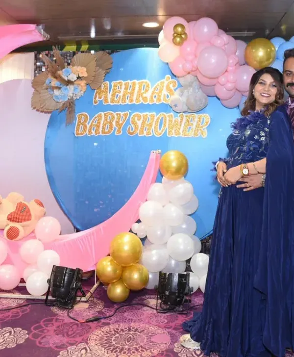 A beautiful portrait of the expecting couple in front of their "Mehra's Baby Shower" decor, featuring a moon and balloon theme.