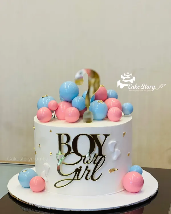 A stylish 'Boy or Girl' gender reveal cake. The clean white cake is decorated with pink and blue spheres and a golden question mark, building excitement for the big reveal.