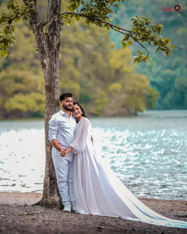 A serene pre-wedding photo of a couple by a lakeside in Uttarakhand. The flowing white dress and natural backdrop create a romantic, ethereal feel, perfect for a destination pre-wedding album.