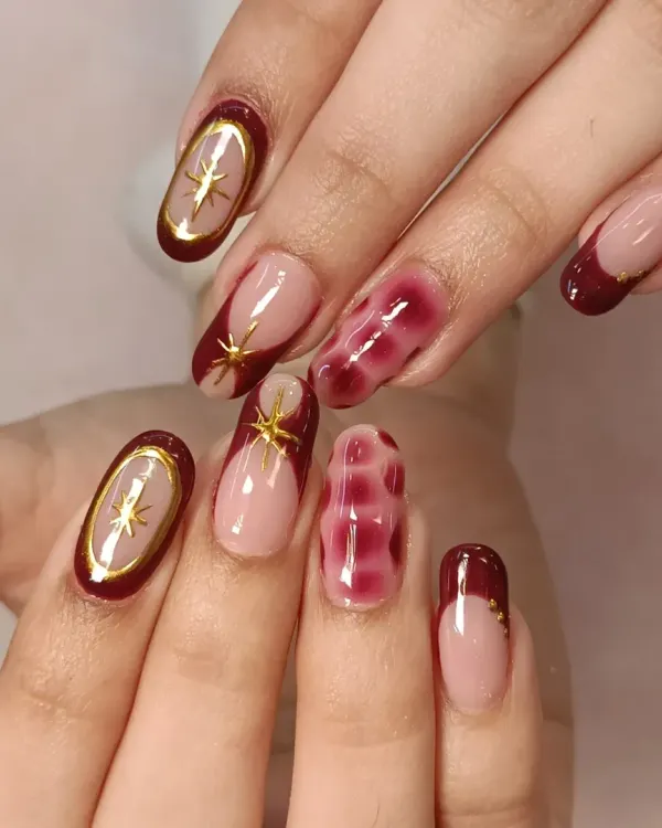 A complete view of this gorgeous set. The design combines deep maroon French tips, a unique blooming gel accent nail, and delicate gold star charms for a celestial-inspired look.