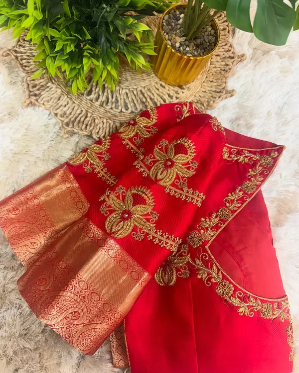 A close up of a bridal red blouse sleeve, showcasing dense floral embroidery in gold thread. The design combines traditional motifs with a modern aesthetic, perfect for a wedding saree.