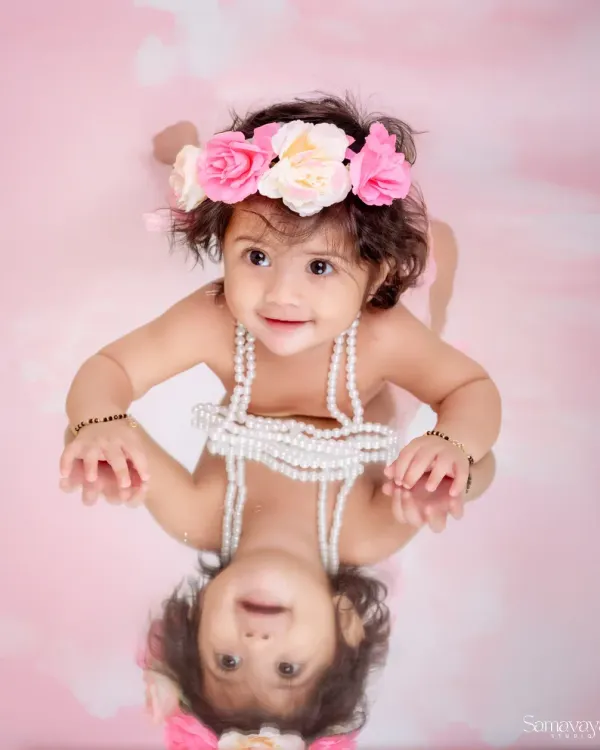 This is a perfect example of a sitter session, capturing the baby's joyful expression and curiosity. Using a mirror creates a playful and unique composition, reflecting her happy smile and celebrating this fun stage of development.