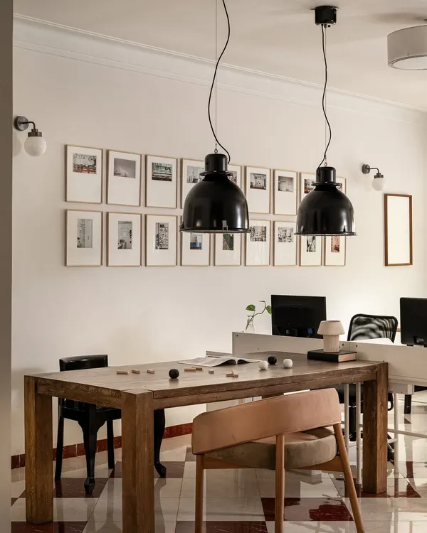 The main collaboration area in our studio, centered around a solid wood table and industrial pendant lights. The gallery wall behind features a collection of images that inspire our work, making this a hub for brainstorming and creative development.