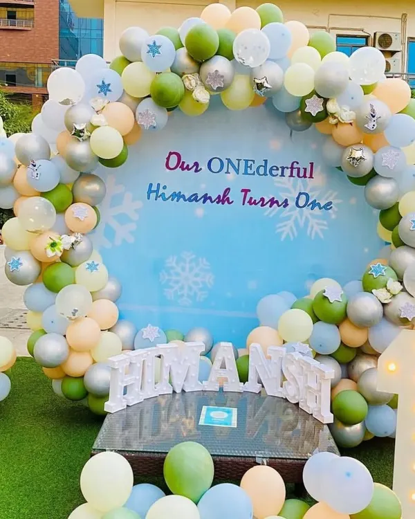 An outdoor first birthday setup with a "ONEderful" winter theme, featuring a circular backdrop and a pastel balloon arch. The large light-up number '1' and personalized name sign add a special touch.