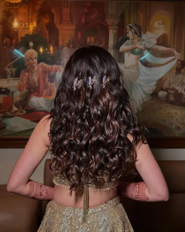 The final look for Ria's sangeet. These voluminous curls have incredible movement and are accented with delicate purple bird clips, adding a touch of whimsy to a glamorous golden lehenga.